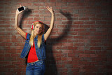 Fototapeta Tematy - Young woman standing at the brick wall and listening to music