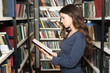 © ImageFlow - young lady standing between book shelves in the library reading