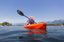 Young Boy Paddling A Kayak On A Beautiful Mountain Lake. Low Angle View Of The Nature's Beauty
