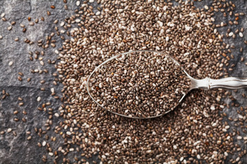 Chia seeds in silver spoon on black table, top view