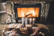 Feet In Woollen Socks By The Christmas Fireplace. Couple Sitting Under The Blanket, Relaxes By Warm Fire And Warming Up Their Feet In Woollen Socks. Winter And Christmas Holidays Concept