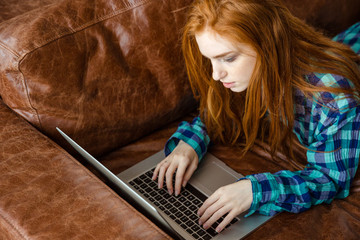 Sticker - Concentrated redhead woman working with laptop and lying on  couch