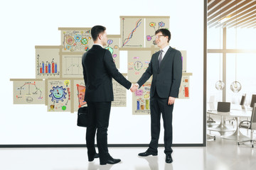 Business partners shake hands at white wall with posters with bu