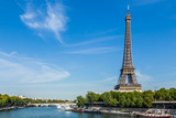 Fototapeta Paryż - Eiffel Tower, Paris, France, September 11, 2015. Shown against a blue sky, with wispy clouds. In the foreground are boats on the river Seine.