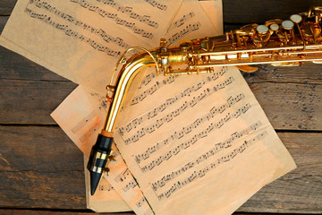 Wall Mural - Beautiful golden saxophone with musical notes on wooden background, close up