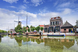 Fototapeta  - Smooth green canal with moored boats and monumental houses in the old town of Gouda, The Netherlands.