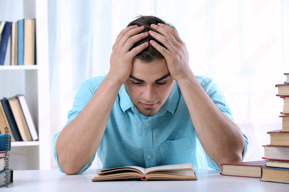 Young man reading book at table in room