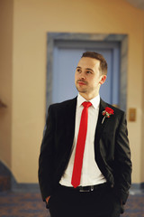 happy handsome smiling groom in black suit with boutonniere posi