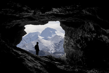 Alone traveller into a cave viewing a snowy mountain landscape,