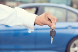 Fototapeta Sawanna - Male hand holding car keys offering new blue car on background