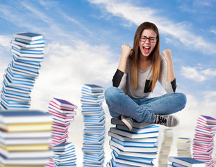 young woman winner sitting on a books tower on the sky