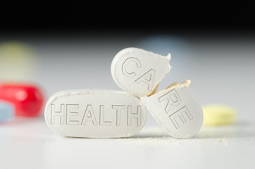 Stack of pills with HEALTH CARE stamped into them, the CARE pill is broken in half representing a broken Health Care system and bad medical care