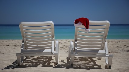 Wall Mural - Santa Claus Hat on sunbed near  tropical calm beach with turquoise caribbean sea water and white sand. Christmas vacation concept