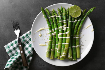 Wall Mural - Fresh asparagus with lime on white plate with checkered cotton serviette on grey table