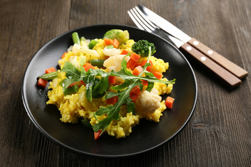 Sticker - Black plate with vegetable risotto, fork and knife on wooden table