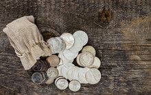Assortment Of Silver Dollars And Half Dollars Spilling Out Of A Small Burlap Bag Onto A Rustic Piece Of Barn Wood.