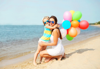 Wall Mural - Mother and child hugging with colorful balloons on beach near se