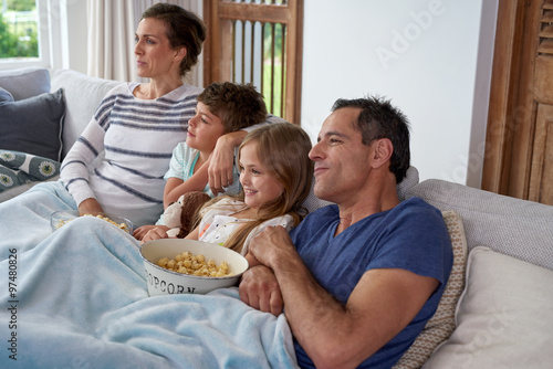 Family Time At Home Snuggling On Couch In Living Room Having Pop