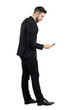 © sharplaninac - Side view of young businessman in suit typing message on smartphone touchscreen. Full body length portrait isolated over white studio background.
