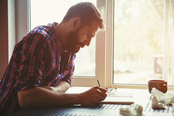 bearded man writing in notebook with pen and paper balls
