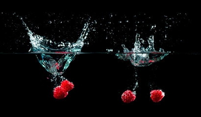 raspberries splash in to water on black background