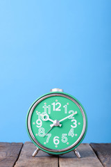 Old green retro clock on wooden table with blue background still life with copy space