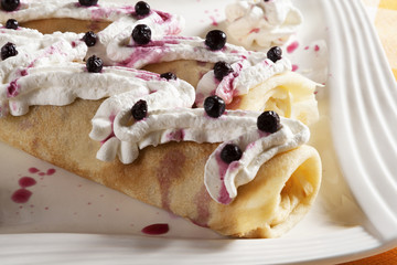 Two pancakes with sweet filling served on a white plate with whipped cream and blueberry.