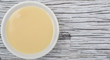 Sweet condensed milk in white bowl over wooden background