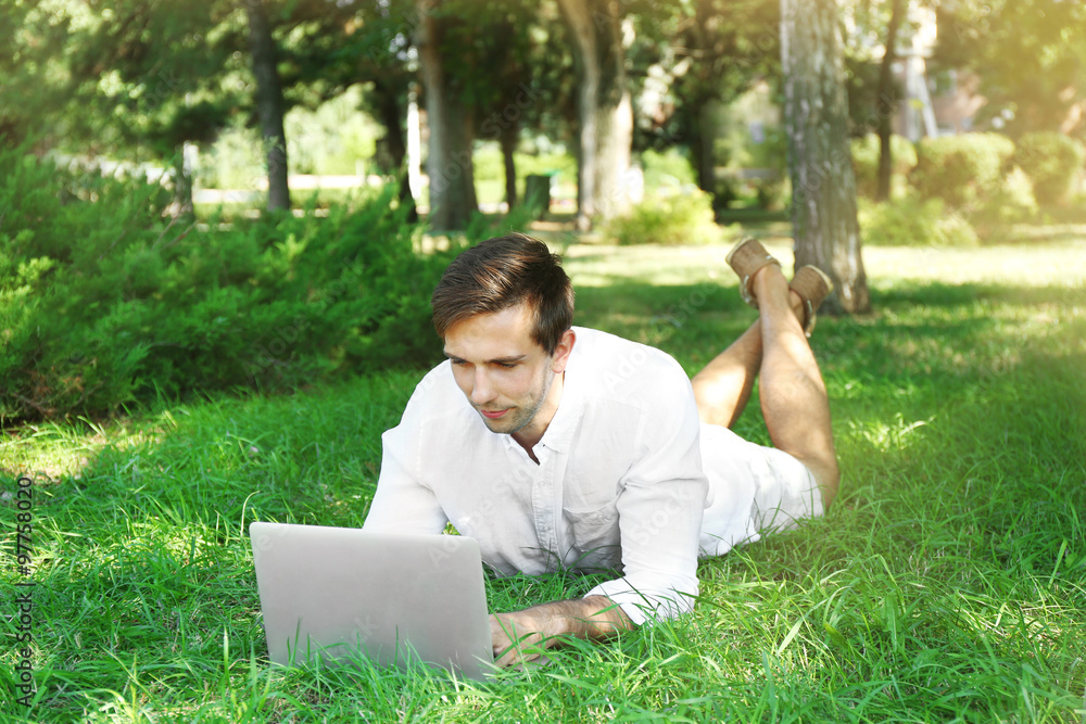 Man with laptop lying on green grass in the park