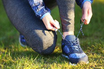 Woman in sportswear tying shoelaces on sneakers outdoor close-up