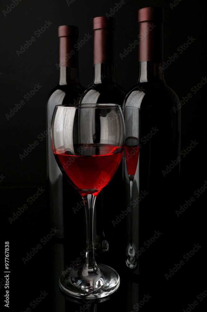 Red wine glass against bottles in a row on black background, close up