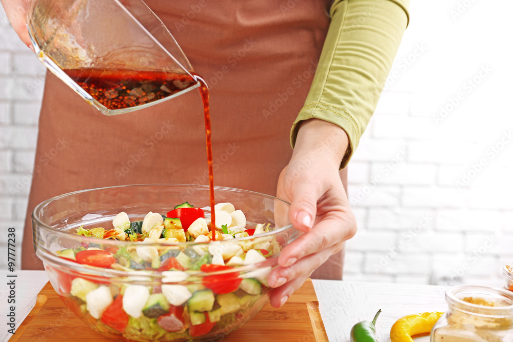 Process of preparing sauce for salad, at kitchen. Woman pouring sauce into glass bowl with salad ingredients