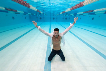 Wall Mural - Man portrait wearing white shirt inside swimming pool. Underwater image.