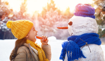 Poster - happy child girl plaing with a snowman on a snowy winter walk