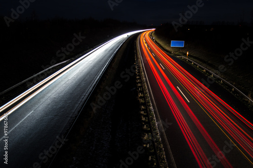 Sentiers de lumière de voiture avec panneau routier bleu, longue exposition Poster Mural XXL