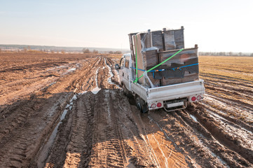 Wall Mural - Off-road truck with furniture settles down in mud on dirty road in fallow field