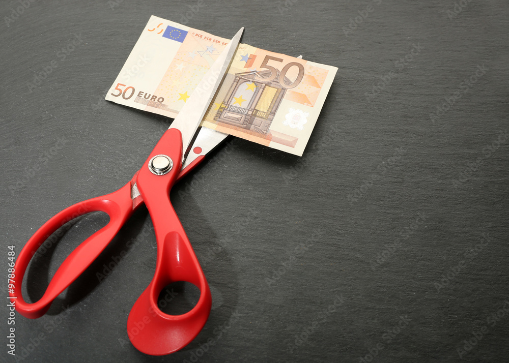 Red scissors cut money on black background. Financial concept