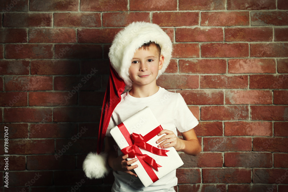 Cute little boy with gift box on brick wall background.