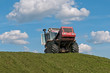 Weeled tractor rams green silo heap on blue sky background. 
