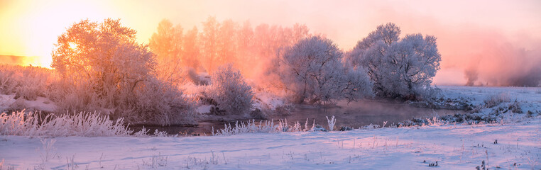 Fairy winter landscape on river . The sun shines through frozen trees . beautiful winter sunrise on lake . stitched panorama . Magic winter sunlight .