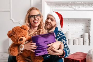 Beautiful couple in Santa hat with gifts by the fireplace. Merry Christmas background