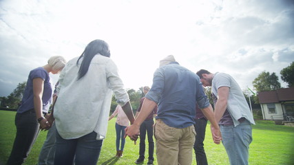 happy christian friends outdoors holding hands in a circle & bowing heads to pray