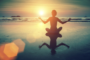 Wall Mural - Silhouette young woman practicing yoga on the sea beach at amazing sunset.