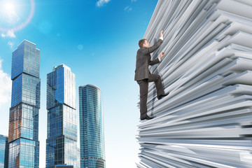 Businessman climbing up a huge stack of paper