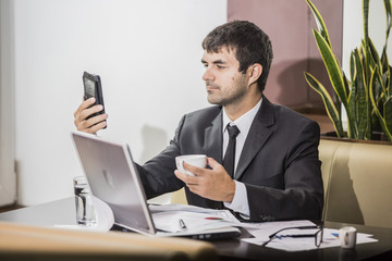 
young businessman working at a laptop sitting at a cafe and holding coffee Cup