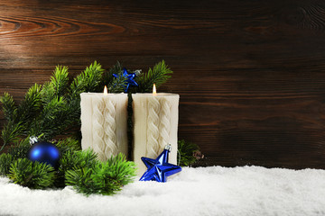 Two grey candles with baubles and fir branch in a snow over wooden background, still life