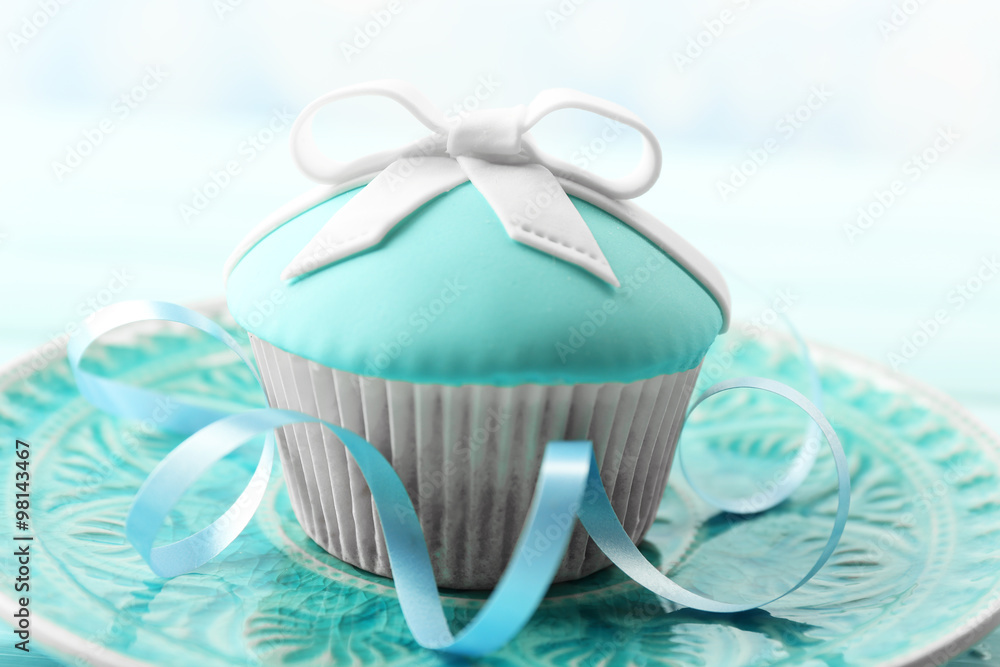 Tasty cupcake with bow on color wooden table, on bright background