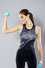 Wall Mural - sporty woman do her workout with dumbbells, isolated on gray bac