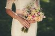 Portrait of a wedding bride posing in a white hipster style dress with flowers in her hands in the forest on sunset
