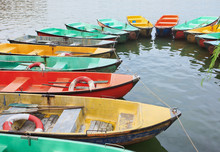 Aged Polyester Multi Colored Row Boats Moored In A Lake.